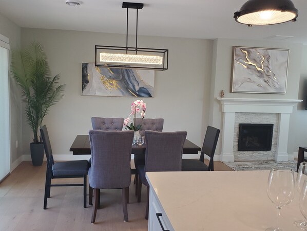 Comedor con una mesa dispuesta para cuatro personas, sillas, una planta en maceta y una lámpara colgante moderna.