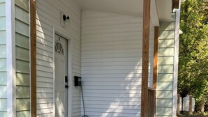 Une véranda en bois avec des marches menant à une porte, un balai et une boîte aux lettres.