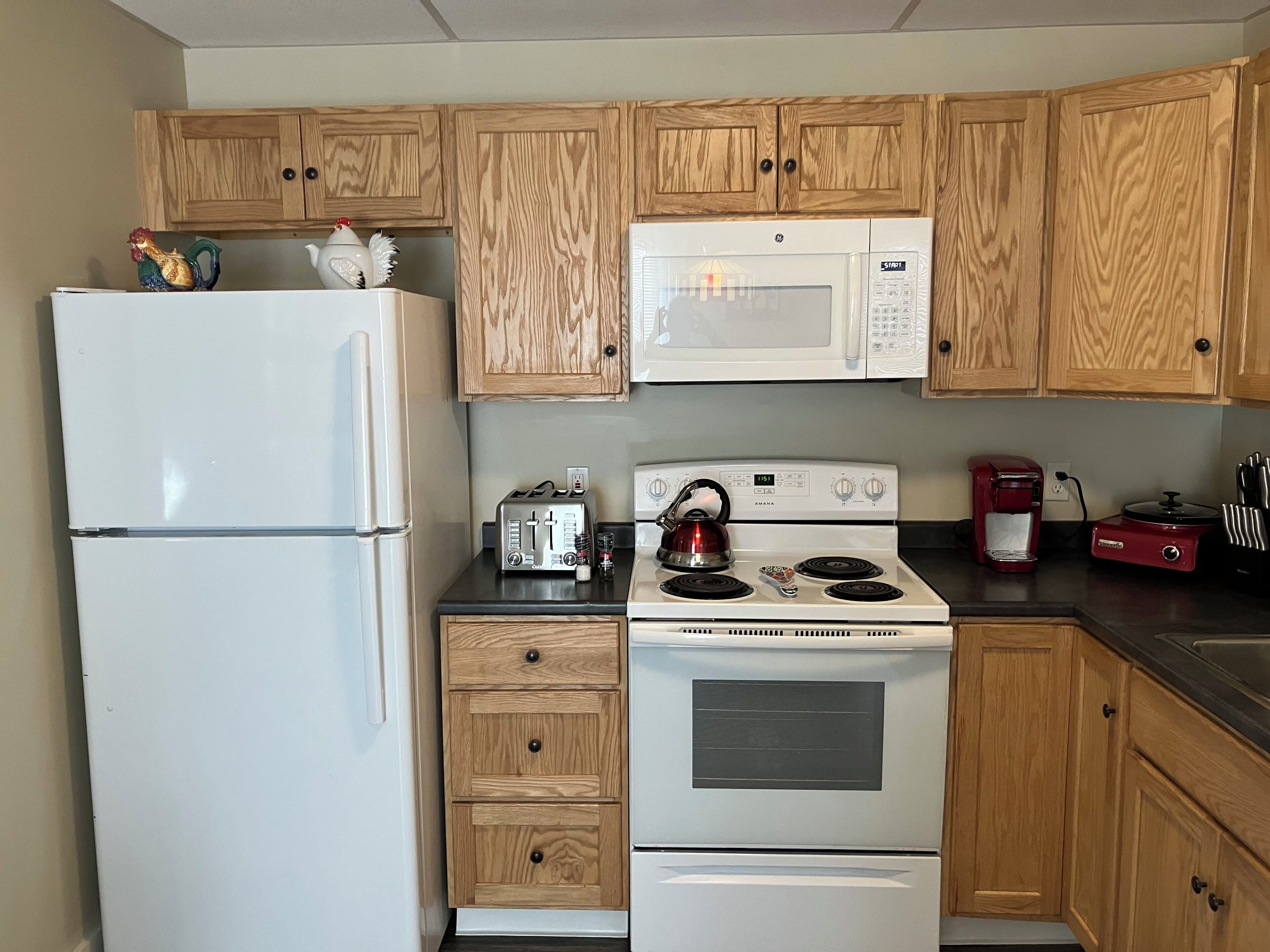 A kitchen with wooden cabinets, a white refrigerator, a microwave, a stove, a toaster, and a coffee maker.