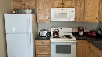 A kitchen with wooden cabinets, a white refrigerator, a microwave, a stove, a toaster, and a coffee maker.