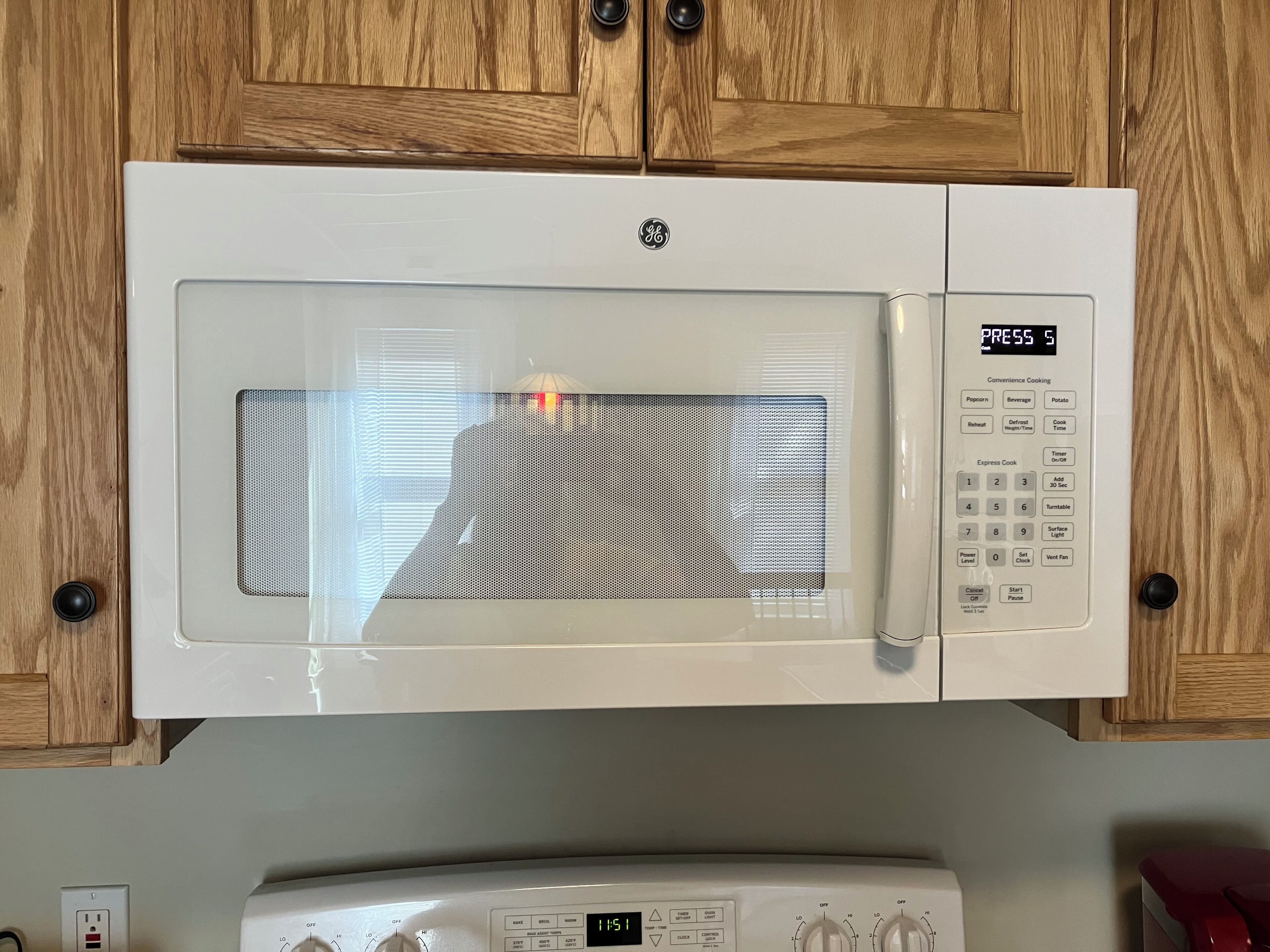 A GE microwave oven with a digital display and control panel, mounted on a wooden cabinet.
