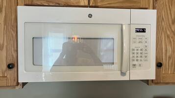 A GE microwave oven with a digital display and control panel, mounted on a wooden cabinet.