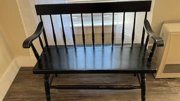 A black wooden bench with a backrest and armrests, positioned in a corner with a window in the background.