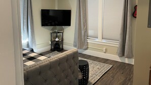 Un salon moderne avec un téléviseur à écran plat fixé au mur, un canapé capitonné, une petite table d’appoint et un tapis à motifs.