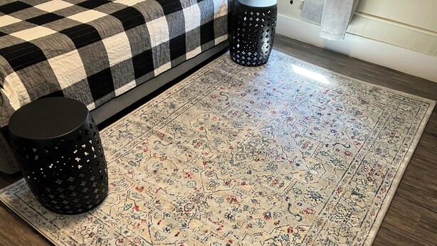 Une pièce avec une couvre-lit à carreaux, un tapis à motifs et deux objets cylindriques noirs.