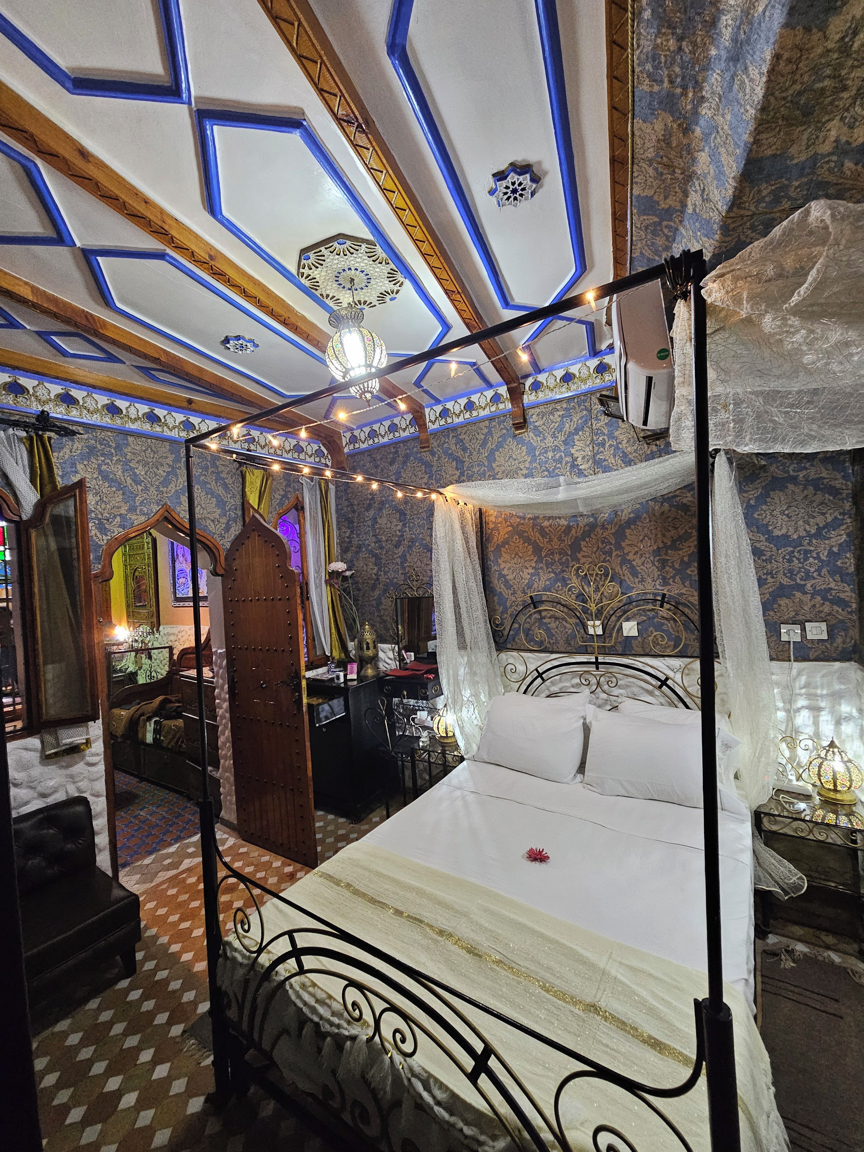 A room with a four-poster bed, a chandelier, and patterned wallpaper.