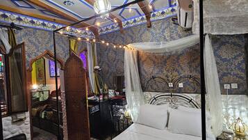 A room with a four-poster bed, a chandelier, and patterned wallpaper.