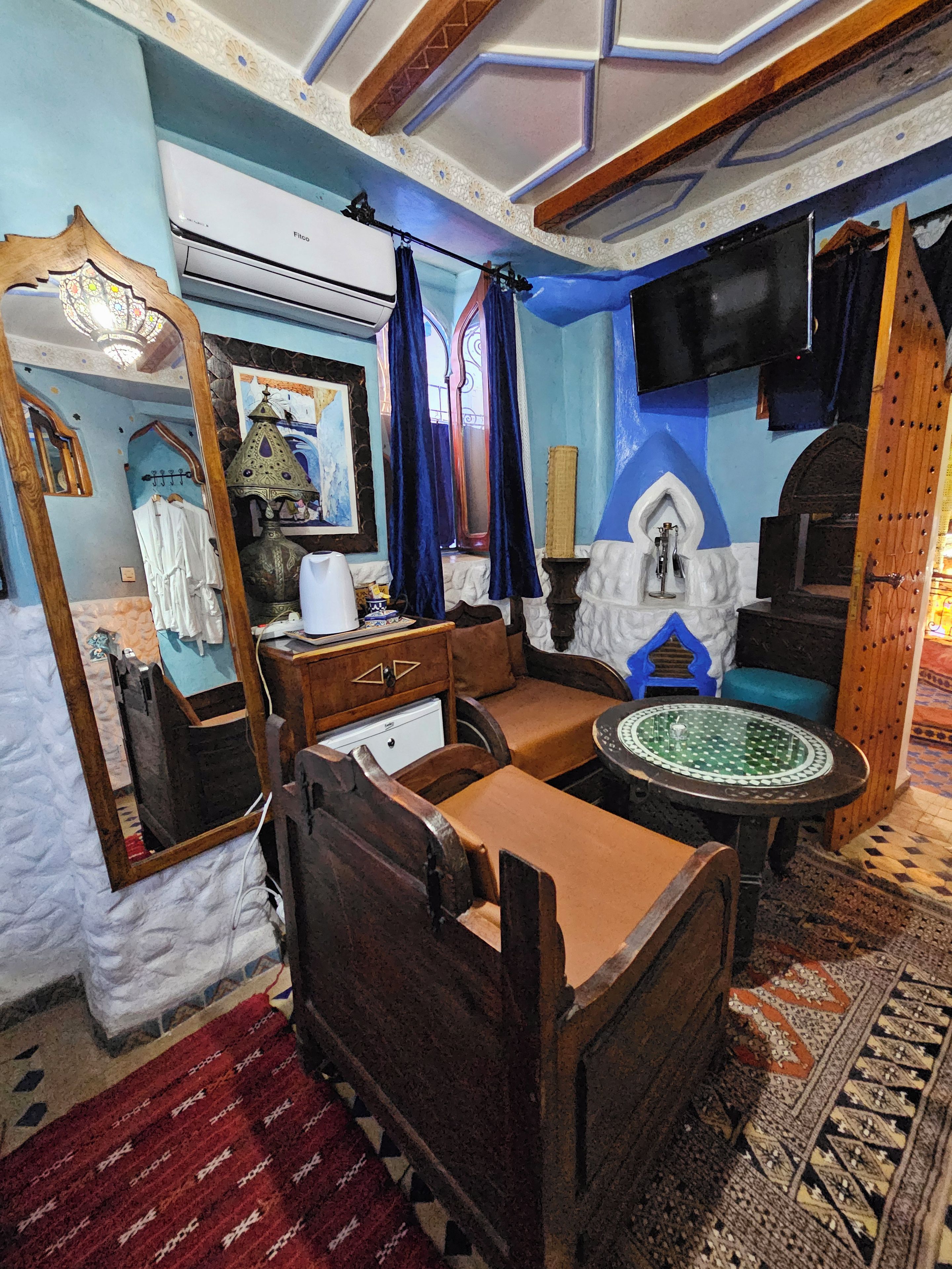 A traditional room with a bed, a small table, a mirror, and a television mounted on the wall.