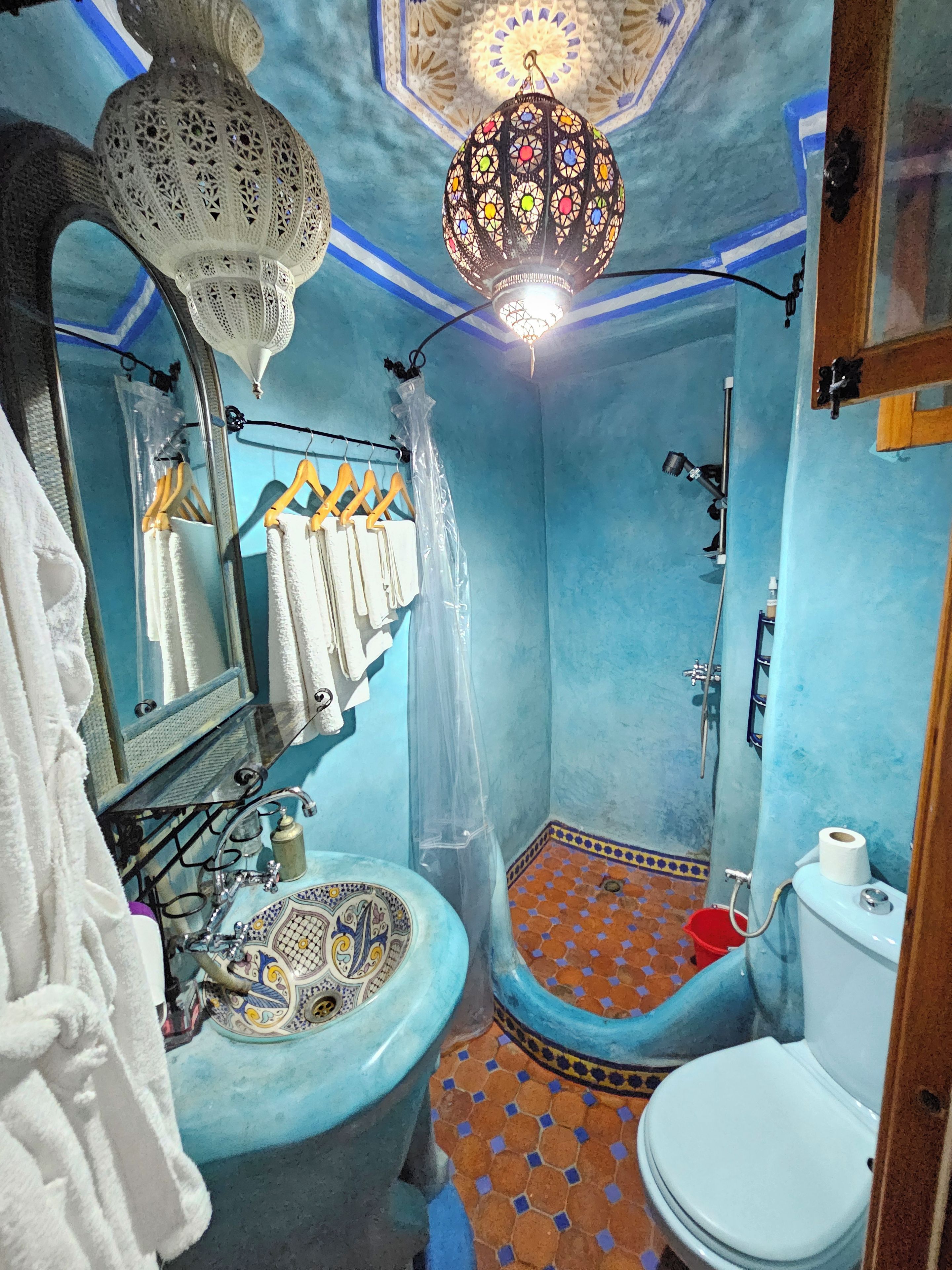 A bathroom with a blue wall, a patterned sink, a toilet, and a shower area.