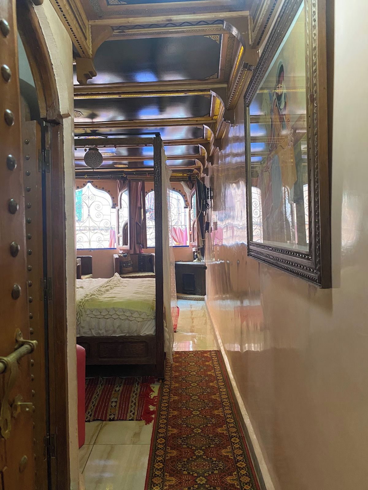 A narrow corridor with a bed and a window, leading to a room with a bed and a window.
