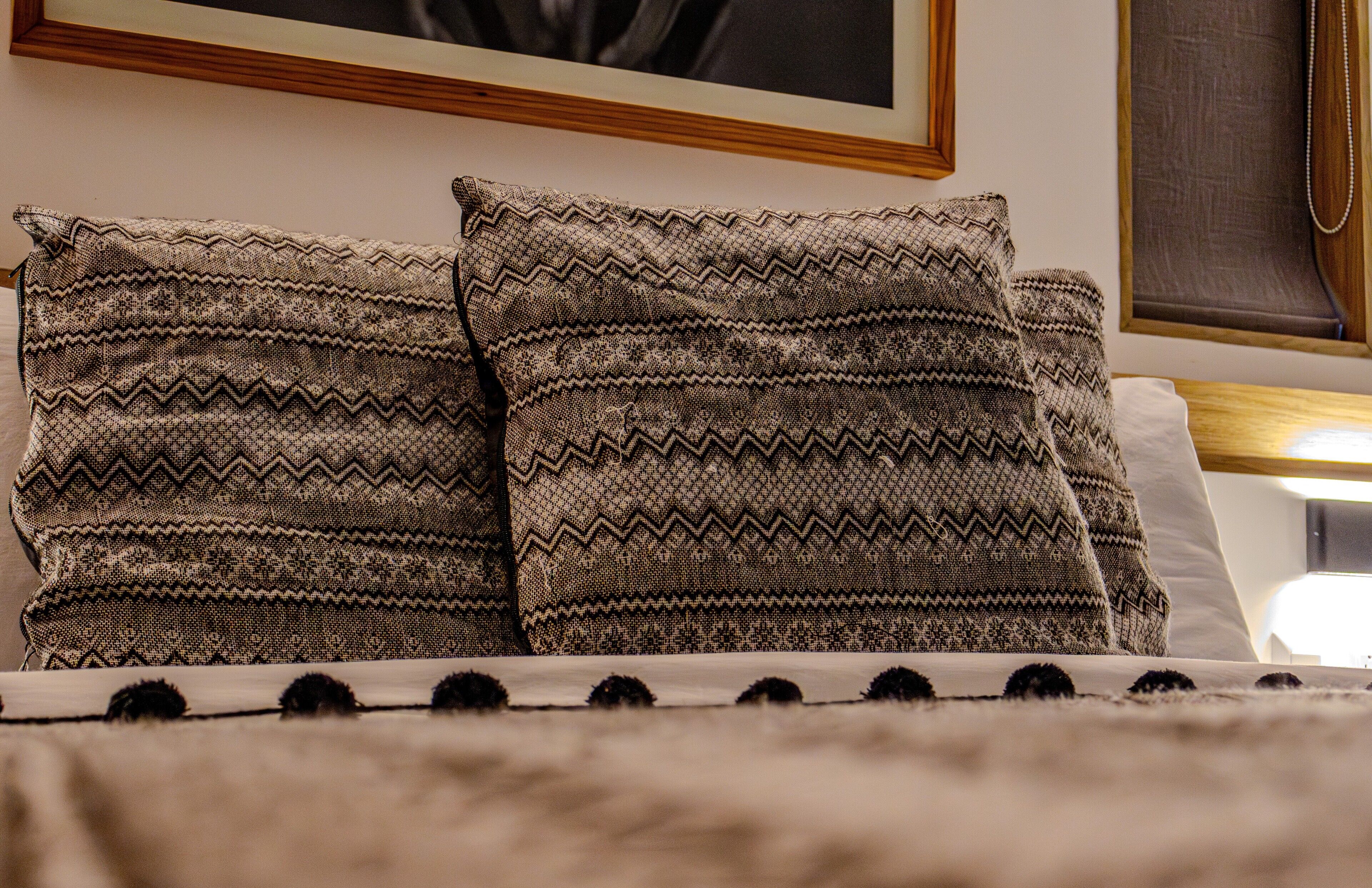 Una cama con almohadillas estampadas y una manta blanca con pompones negros.
