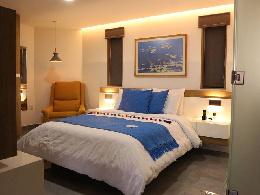 Une chambre d’hôtel avec un grand lit, une chaise, un tableau au mur et des lampes de chevet.