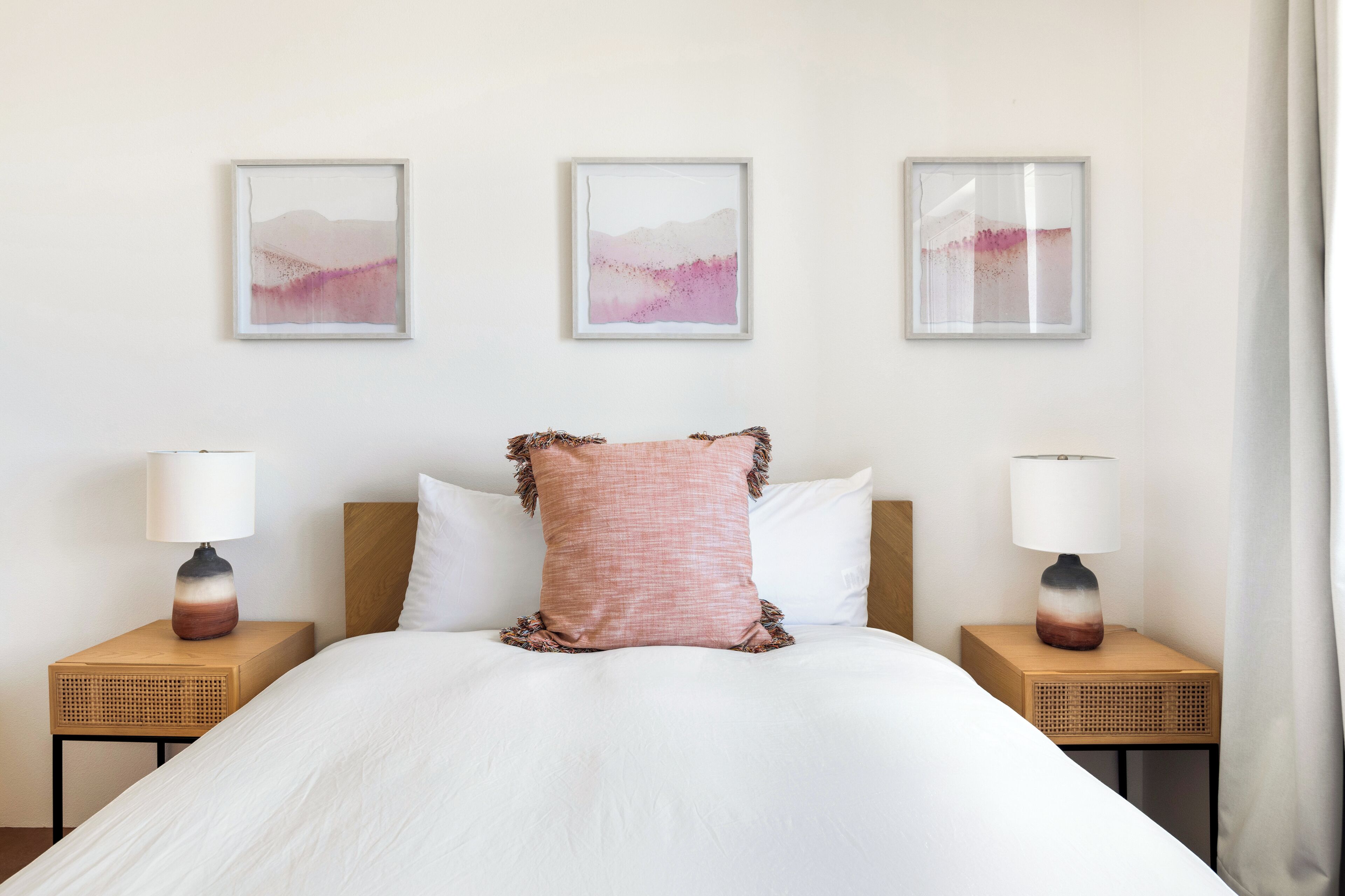 Una camera d'albergo ordinata con un letto grande, due comodini con lampade e tre opere d'arte incorniciate appese al muro.