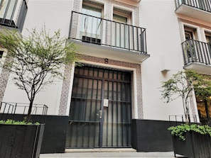 A multi-story building with a black and white facade, a large central entrance with a metal gate, and balconies with black railings.