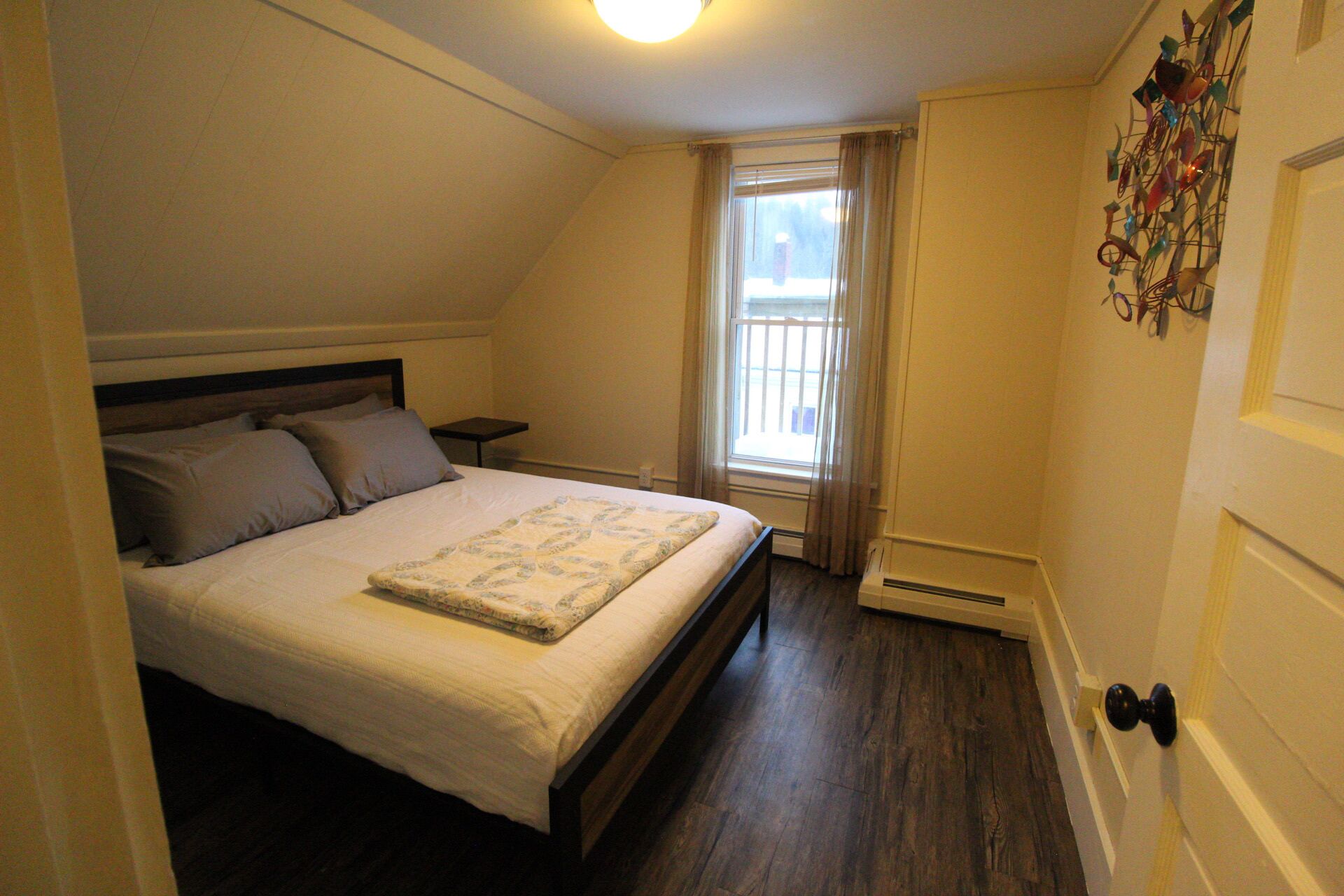A bedroom with a bed, a nightstand, a window with curtains, and a radiator.