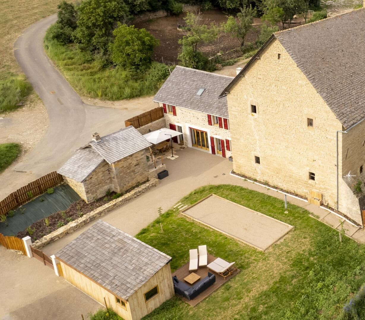 Un grand bâtiment en pierre doté d’une cour, d’une structure en bois et d’un espace pavé aménagé avec du mobilier d’extérieur.