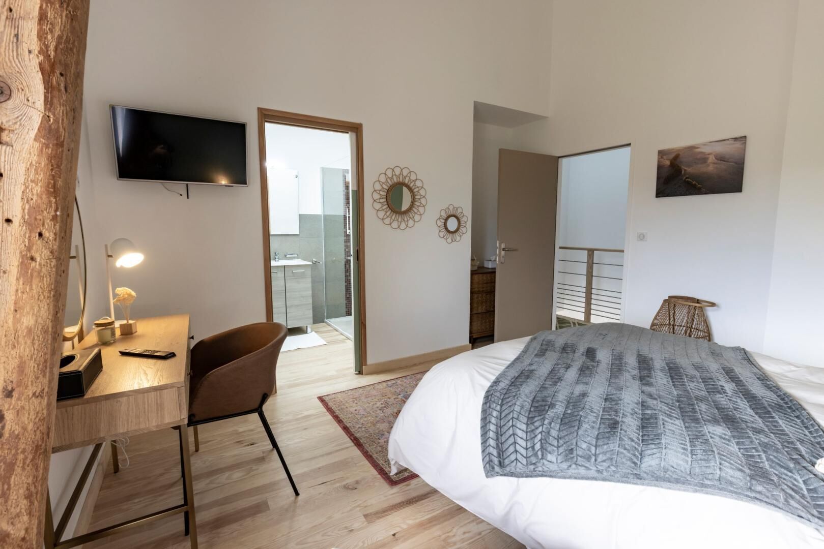 Un dormitorio con cama, escritorio con silla, televisor y puerta que da a un balcón.