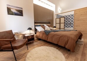 Una camera da letto con un letto, una sedia, un comodino, una lampada e un quadro appeso al muro.
