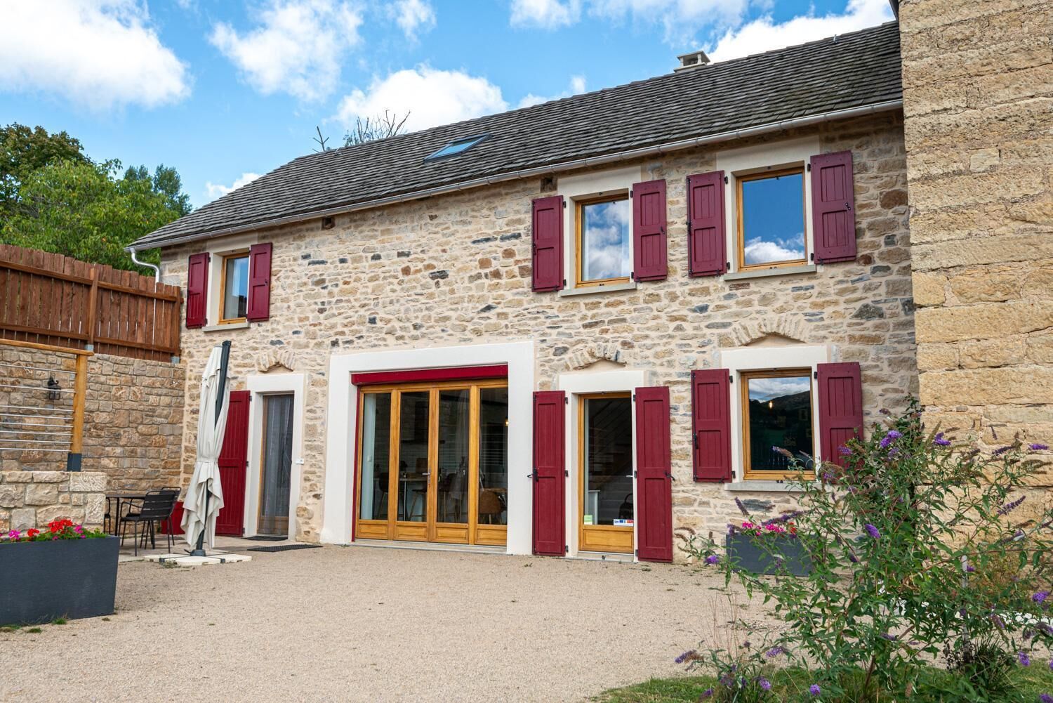 A stone building with red shutters, a wooden door, and a gravel driveway.