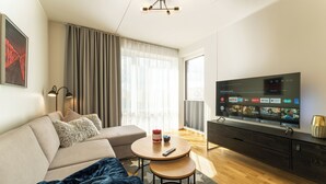 A modern living room with a sofa, a round coffee table, a TV, and a large window with curtains. - Citygate Sunset Balcony (Tartu)