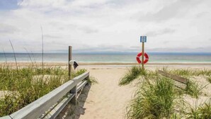 A beach path leading to the ocean with a lifebuoy and a signpost.