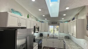 A modern kitchen with white cabinets, granite countertops, stainless steel appliances, and a skylight.
