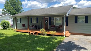 Relax on the covered porch with two chairs and a bench, surrounded by a well-maintained lawn and a small tree.