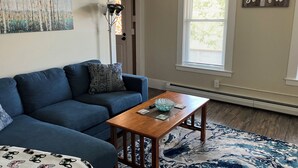 A living room with a blue sofa, a wooden coffee table, and a patterned rug. - Lots of Space for a Great Price! Barre VT! (Barre)