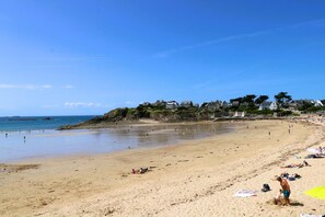 A wide sandy beach with people sunbathing and swimming, houses on a cliff in the background, and a clear blue sky. - A Saint-malo, Dans le Quartier de Rochebonne et à 1.8km du Bourg de Rothéneuf, Agréable Location de (SAINT MALO)