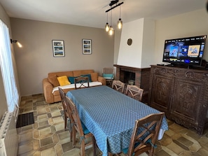 Ein Wohnzimmer mit Sofa, Esstisch, Stühlen, Kamin und Fernseher.