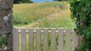 A stone archway with a white picket fence leading to a grassy field and a view of the sea.