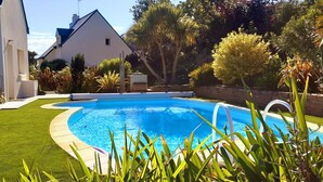 A swimming pool surrounded by a well-maintained lawn, with a house in the background.