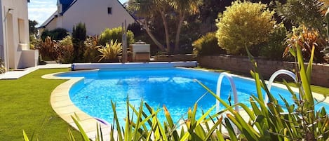 En swimmingpool omgiven av en välskött gräsmatta, med ett hus i bakgrunden.