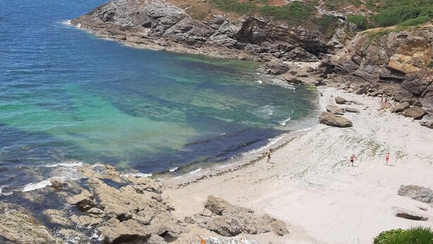 A rocky coastline with clear blue waters and a sandy beach.
