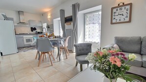 Una cocina moderna con comedor, un sofá gris y un arreglo floral sobre una mesa.