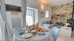 Un comedor con una mesa dispuesta para el desayuno, una pared de piedra y una zona de estar acogedora con sofá y cojines.