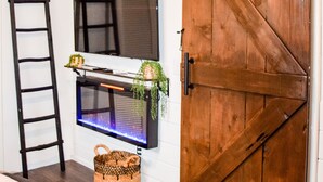 A bedroom with a wooden sliding door, a TV mounted on the wall, a ladder, and a basket on the floor. - Coyote Creek Ranch + Pool House near Murphy’s (Vallecito)