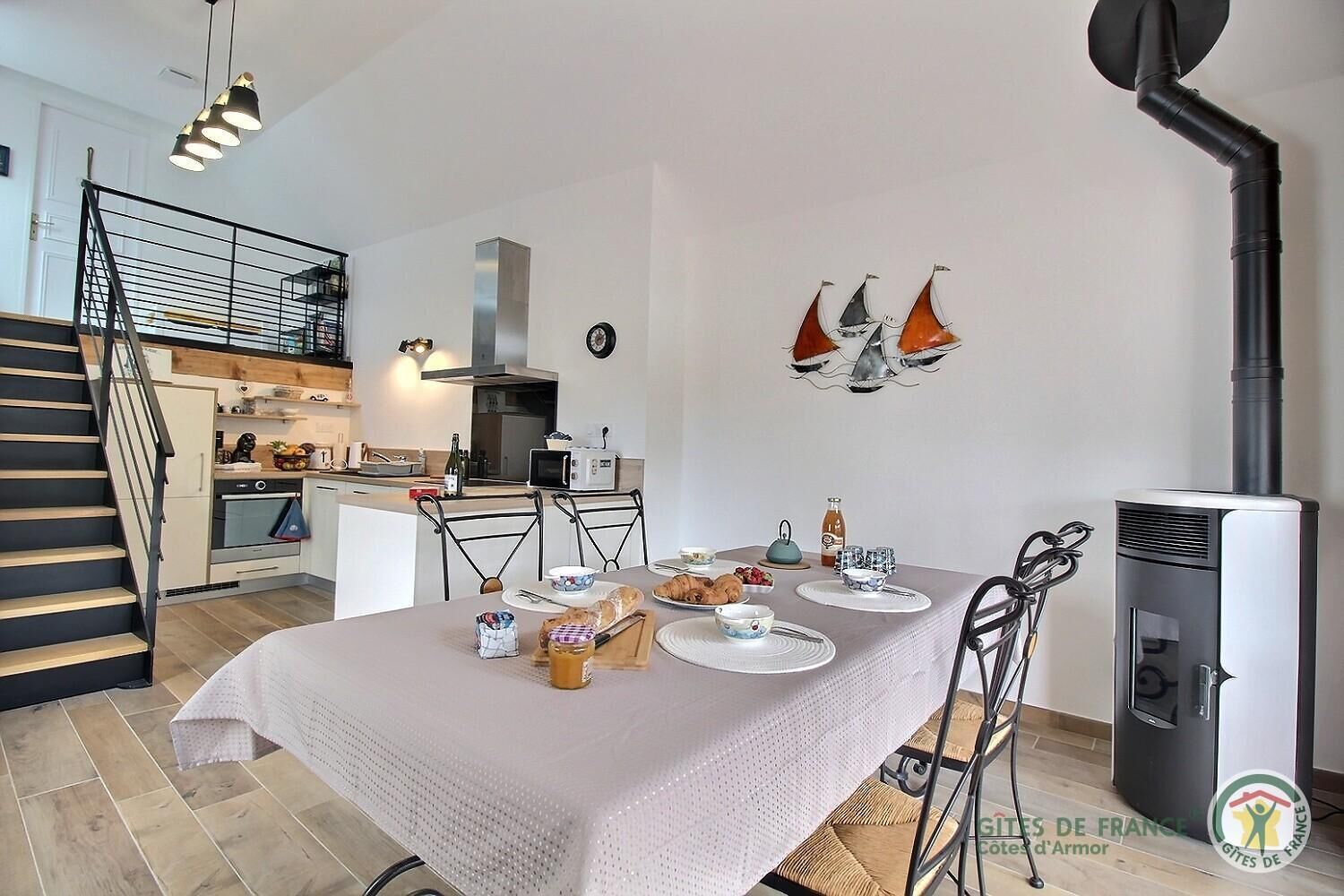 Une cuisine moderne avec une table à manger dressée pour le petit-déjeuner, un escalier et un poêle à bois.