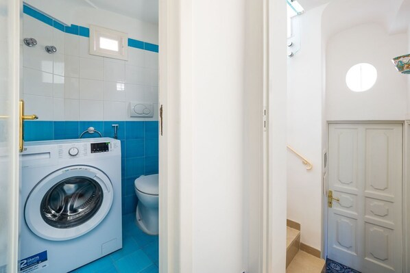 Une petite salle de bain équipée d’un lave-linge, de toilettes et d’une porte dotée d’une fenêtre ronde.