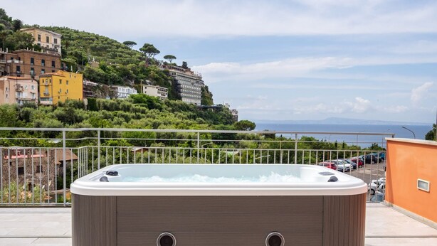 Un jacuzzi en un balcón con vistas a un pueblo en la ladera y al mar.