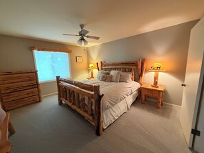 A bedroom with a wooden bed, two bedside tables with lamps, a ceiling fan, and a window with blinds. - Beautiful lake home on the sandy south shores of Pelican Lake. (Nisswa)