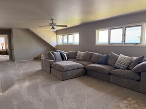 A living room with a sectional sofa, a ceiling fan, and large windows. - Beautiful lake home on the sandy south shores of Pelican Lake. (Nisswa)