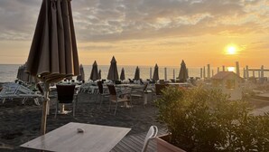 Een restaurant aan het strand met terras, parasols en uitzicht op de ondergaande zon boven de oceaan.