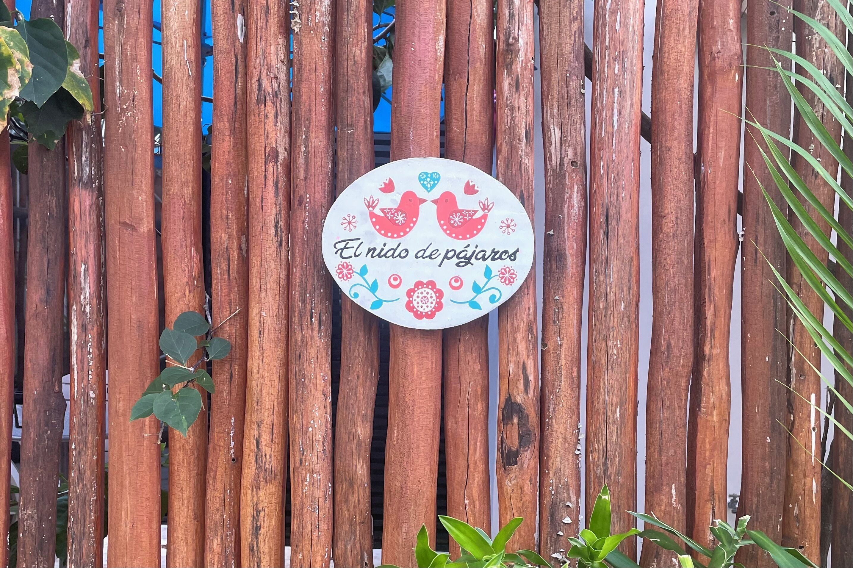 Une clôture en bois sur laquelle est fixé un panneau circulaire orné d’oiseaux et de fleurs décoratives.