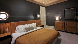 Une chambre à coucher comprenant un lit, une tête de lit en bois, des tables de chevet, une commode, un ventilateur de plafond et des luminaires fixés au mur.