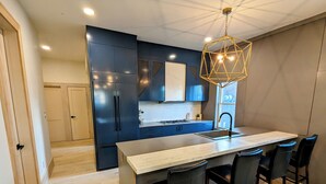 Une cuisine moderne avec des meubles de couleur bleu foncé, un îlot central doté de tabourets de bar et un luminaire suspendu aux motifs géométriques.