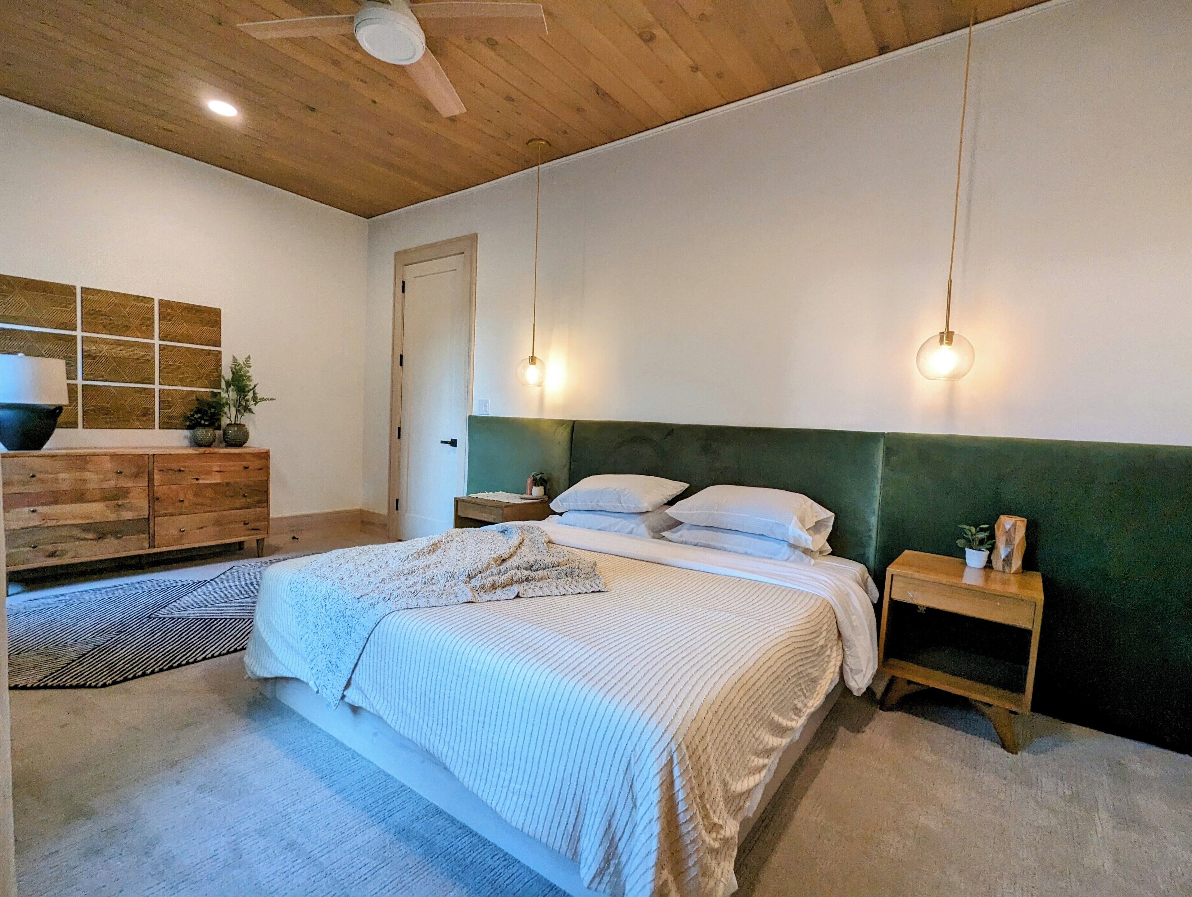 A bedroom with a bed, wooden headboard, bedside tables, a dresser, and a ceiling fan.
