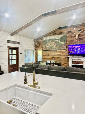 A modern interior with a kitchen area, a seating area with a fireplace, and a mounted deer head. - 55 ACRE PRIVATE WATERFRONT RETREAT~HOTTUB~FISHING~KAYAK~TRAILS~FIRE PIT🔥 (Columbia)