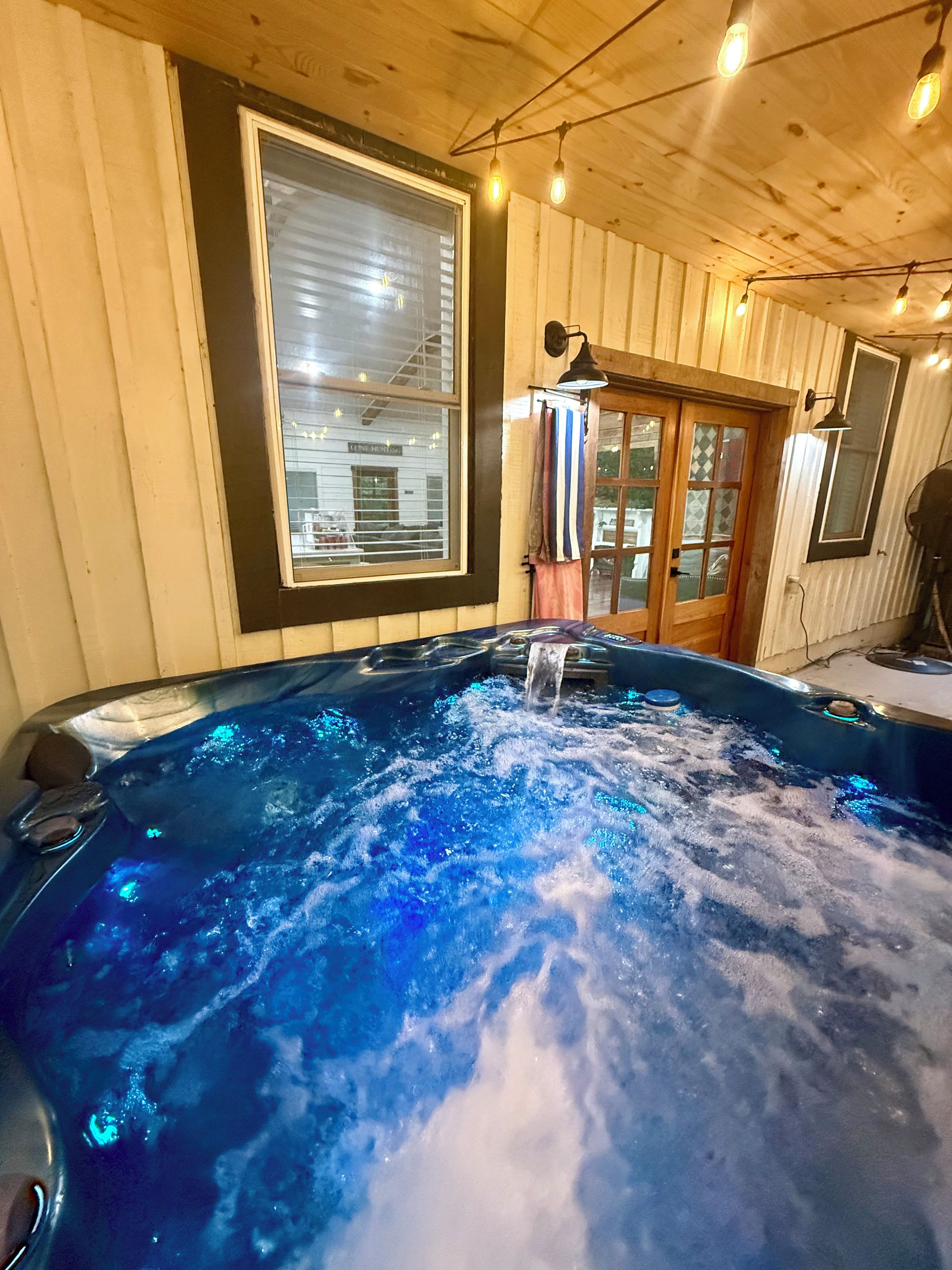 A hot tub with a wooden interior, a window with blinds, and a door with curtains.