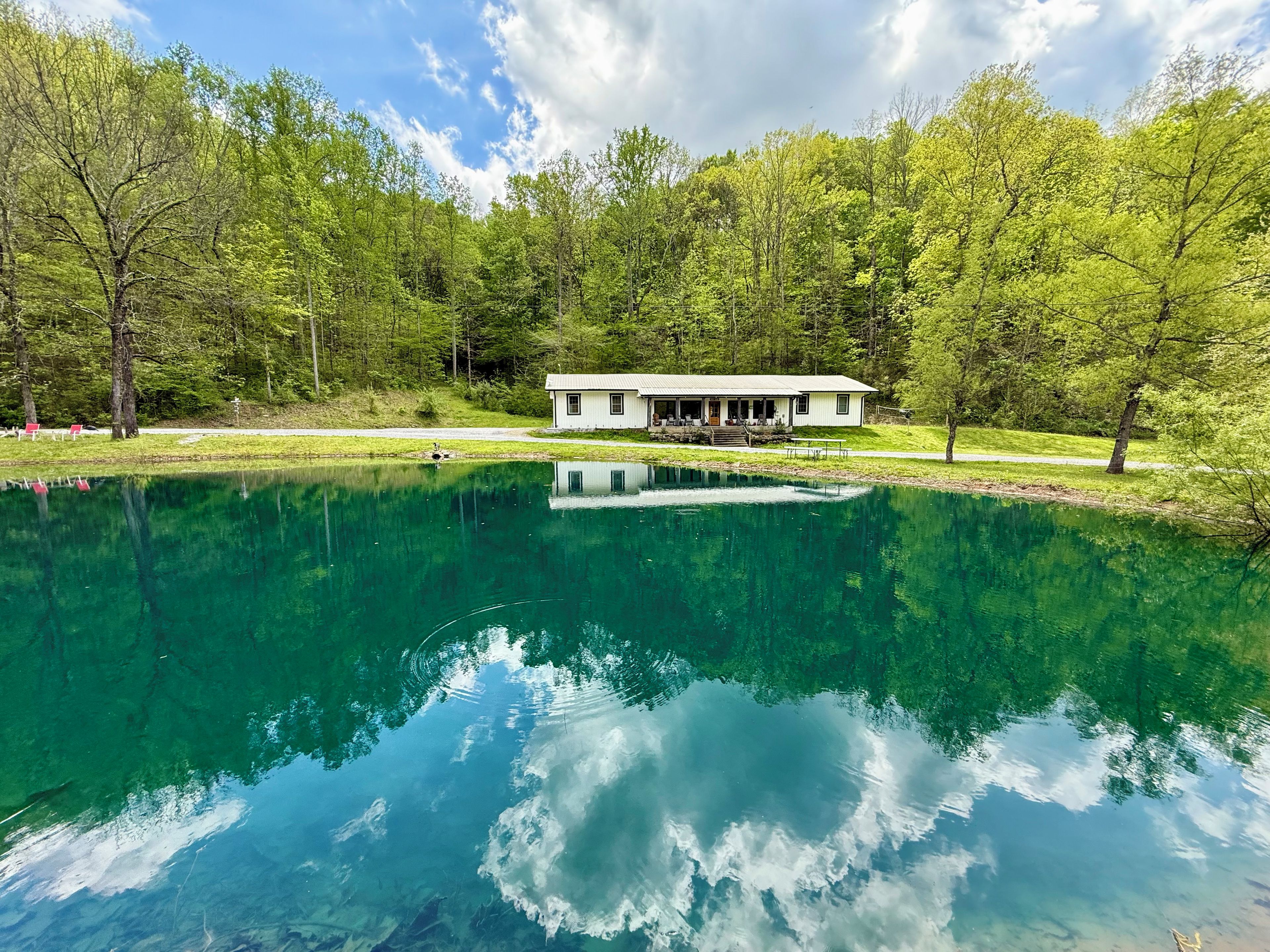 A house with a porch overlooking a clear lake, surrounded by trees.